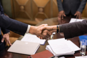 corporate business owner handshake over board room table papers