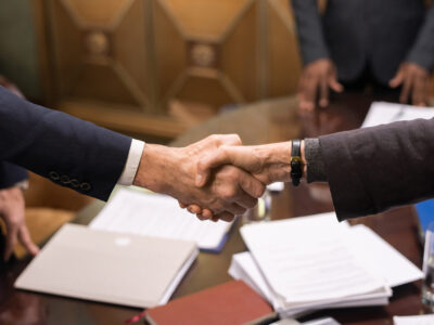 corporate business owner handshake over board room table papers